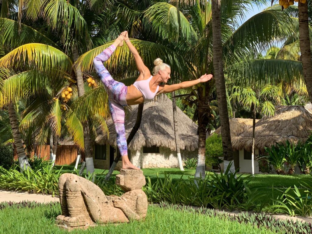 A woman standing on a rock in a yoga pose, surrounded by nature